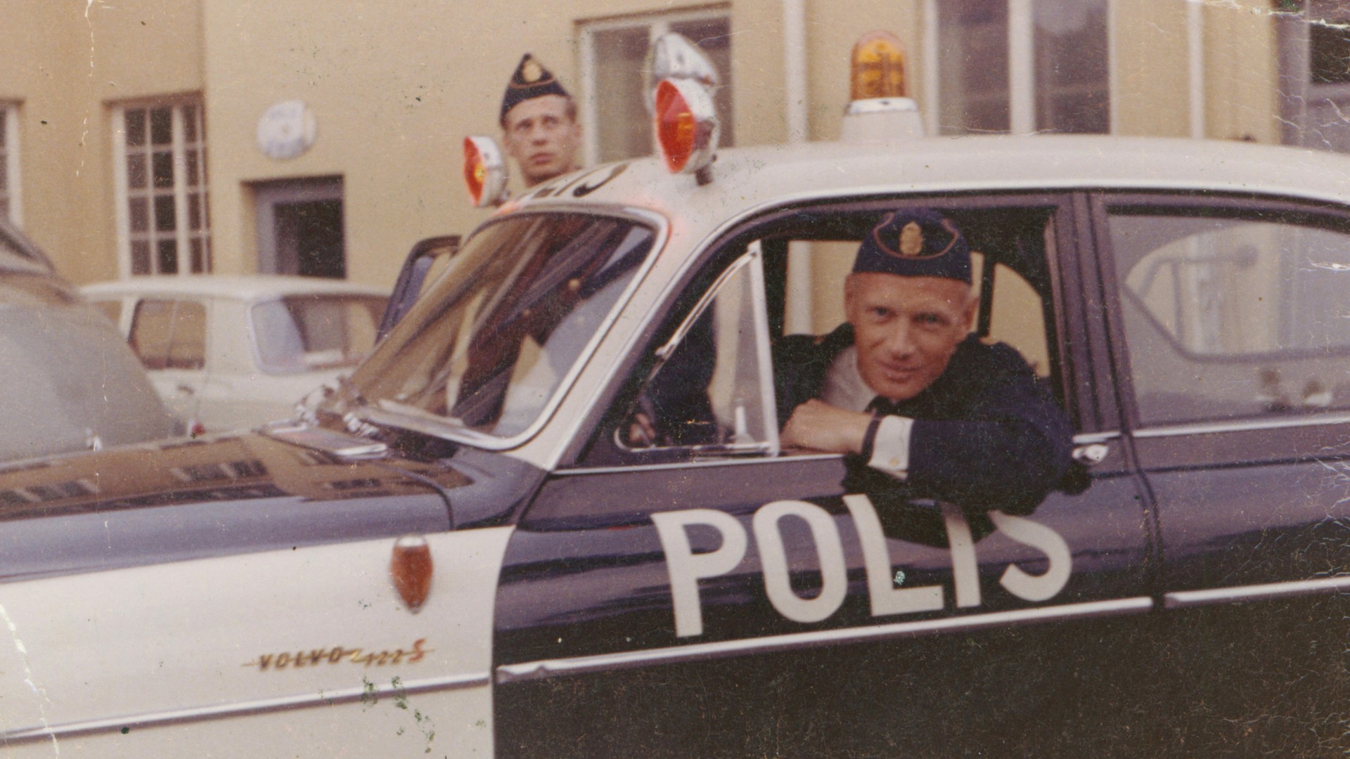 En polis tittar ut ur en polisbil.