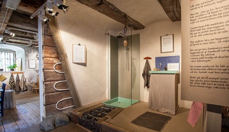 Ett badrum, med lergolv och lerväggar där stockarna syns.