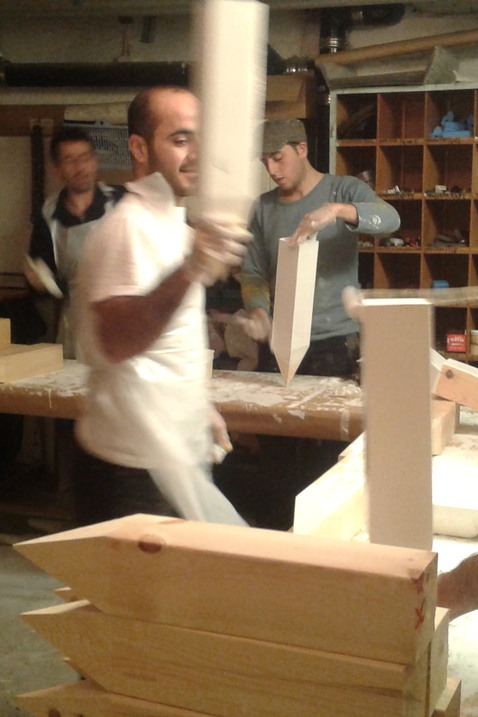 Tre personer på asylboendet Solbacka tillverkar stolpar av trä till konstverket ”Svenska Flaggan”.