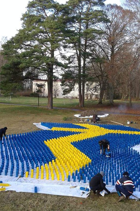 Trästolparna målade gula och blå står nedtryckta i marken i form av svenska flaggan.
