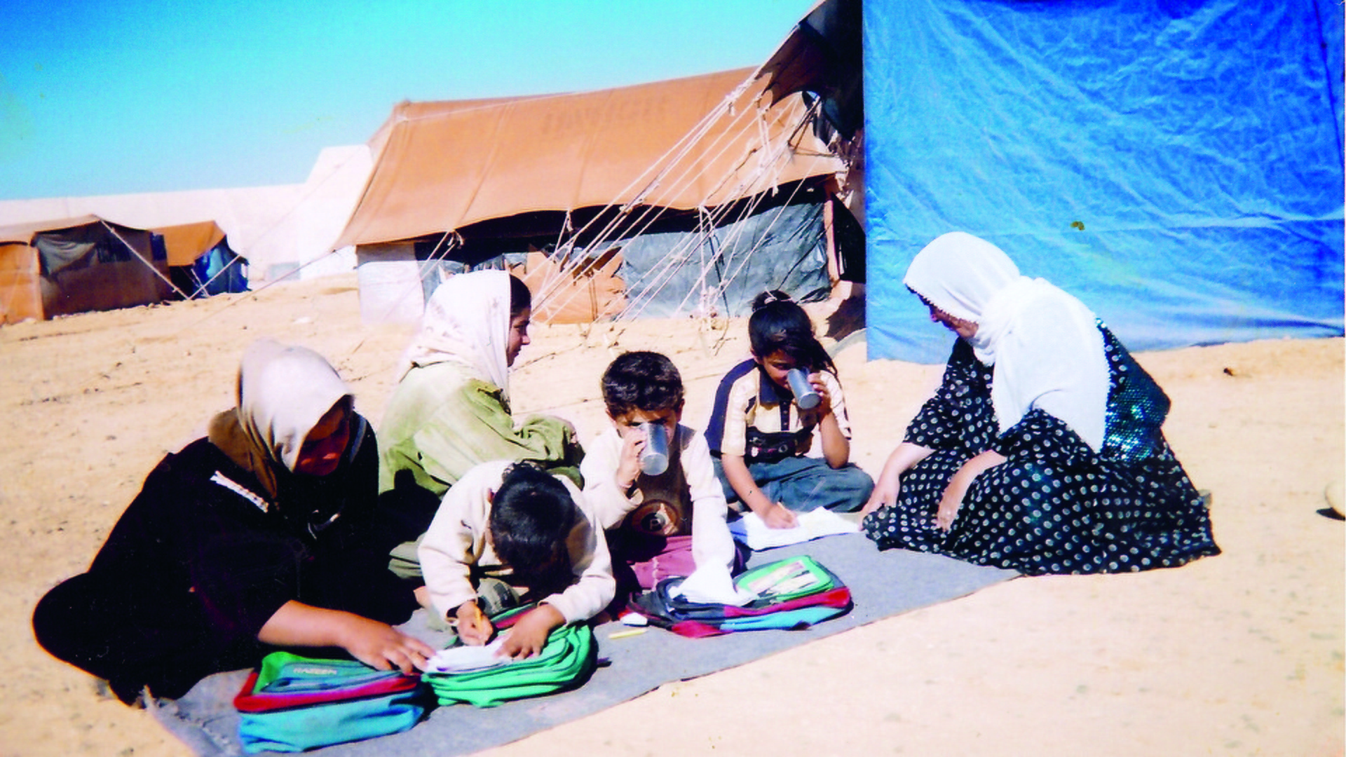 Kvinnor och barn sitter på marken framför ett par tält.