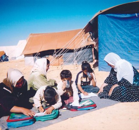 Kvinnor och barn sitter på marken framför några tält
