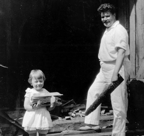 En man, klädd i vitt och en liten flicka i vit klänning bär på vedträn