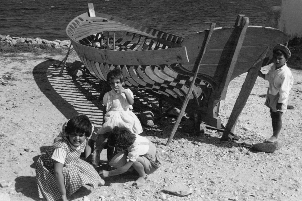 Fyra barn i femårsåldern leker i strandkanten intill en båt-stomme