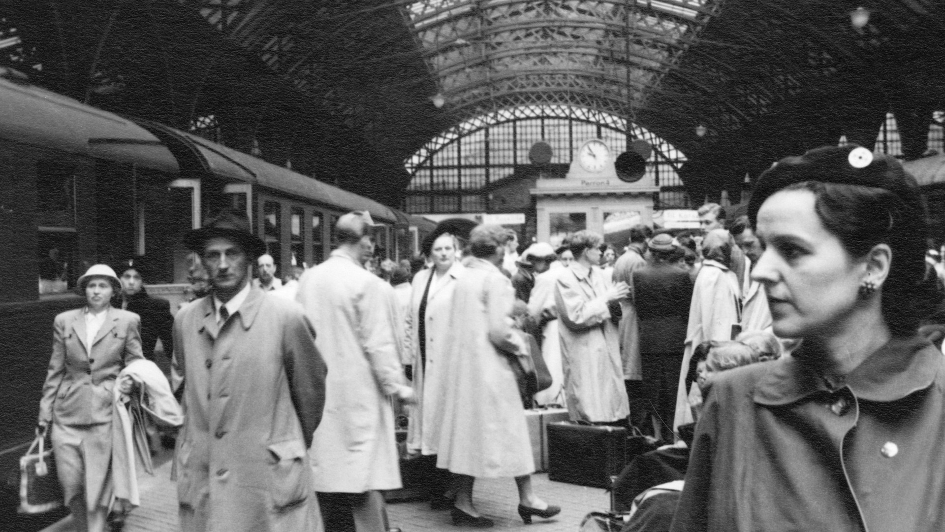 I bildens högra hörn står en kvinna iklädd basker och tittar mot ett tåg som löper längsmed perrongen, på vilken hon befinner sig. Bakom henne är ett virrvarr av människor i kappor och hattar, med resväskor och portföljer.