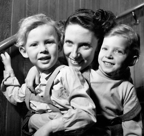 En ung kvinna sitter i en trappa med två små barn i famnen. De ser alla väldigt glada ut. 