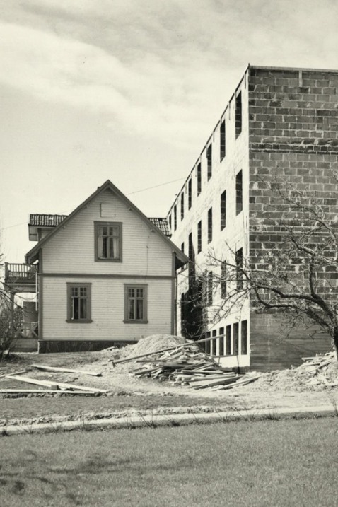 Ett gammalt trähus står framför en ett flervåningshus som är under uppbyggnad. 