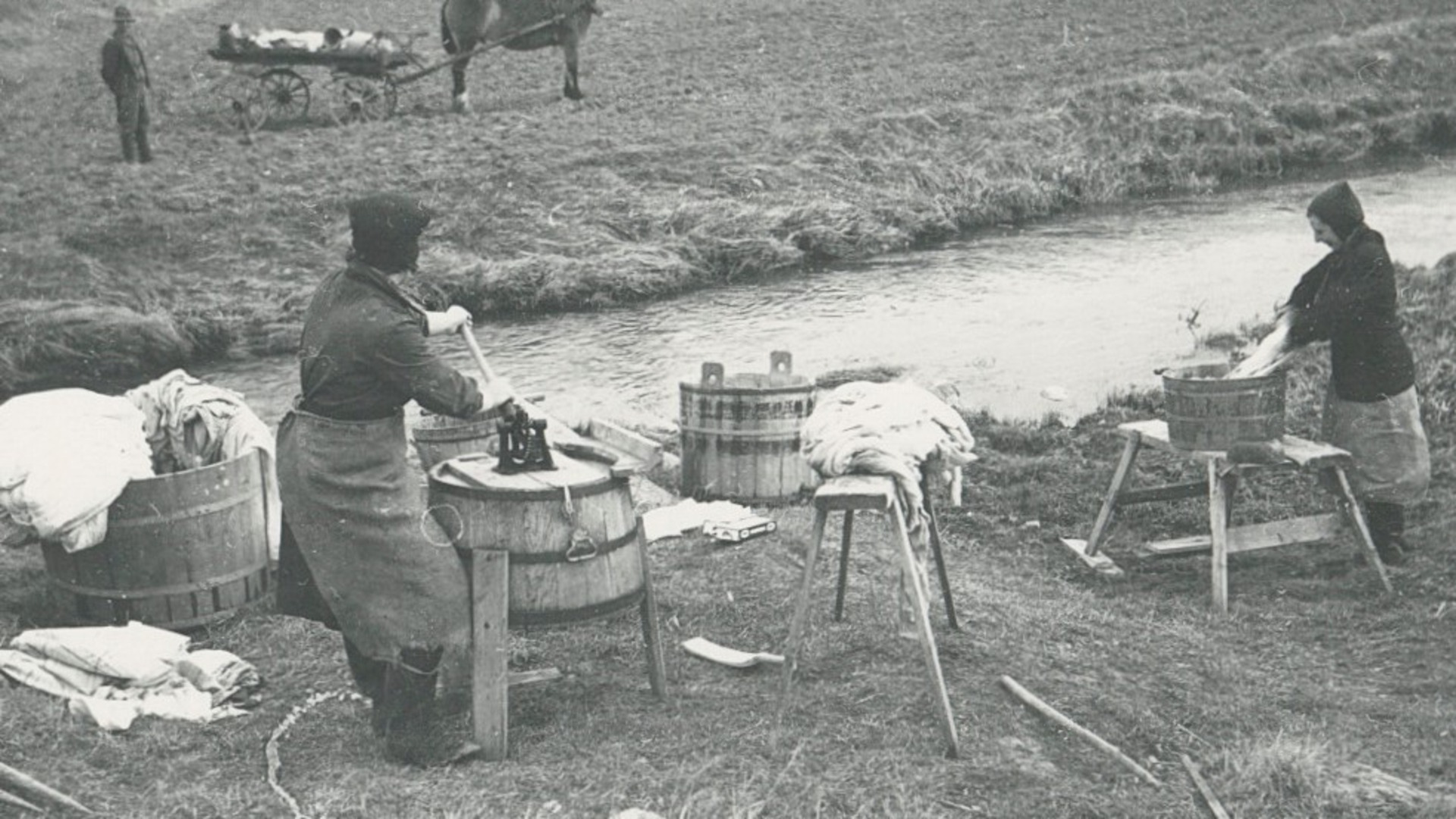 Två kvinnor tvättar vid en å. 