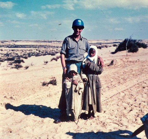 En soldat med två beduinbarn framför sig, i öknen