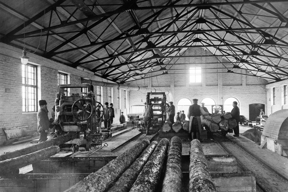 Ett svart-vitt foto på ett sågverk. Några arbetare lastar virke.