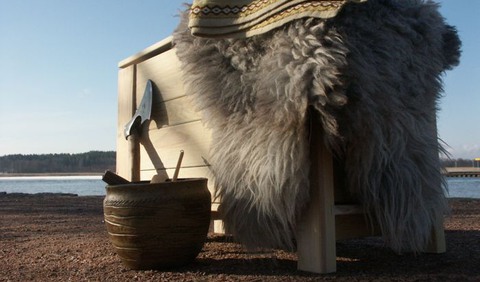 Vikingakistan med fårfäll och filt över. Jämte står en kruka med en yxa i.